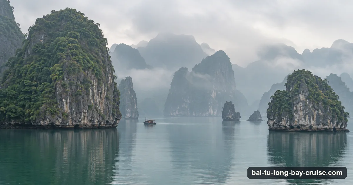 Karst islands fading into winter mist over still water with a small boat in the distance in Ha Long Bay